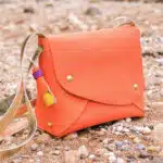 Sac à bandoulière en cuire orange posé sur le sable