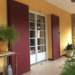 Porte d'entrée avec volets couleur lin de vin, sur mur jaune.