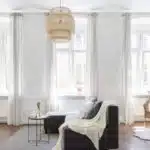 Grandes fenêtres blanches, canapé noir avec drapé blanc et table basse