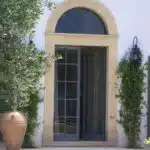 Porte d'entrée entrouverte pot en terre et arbuste à côté.