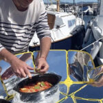 Homme cuisinant avec un four solaire devant un bateau
