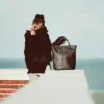 Femme de dos contre un muret face à la mer avec un sac noir
