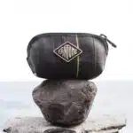 Pochette noir en matière recyclé posée sur un caillou