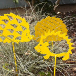 3 hérissons en fer, peints en jaune dans un jardin