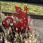 Lézard en fer, peint en rouge dans fleurs