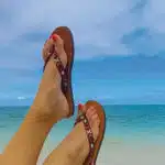 une paire de tongs marron porté sur 2 pieds nus sur fond de mer
