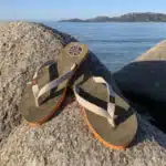 une paire de tongs couleur kaki et semelle orange, courroie blanche,posée sur un rocher