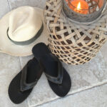 une paire de tong noire, un chapeau panama et un photophore posés sur du carrelage