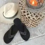 une paire de tong noire, un chapeau panama et un photophore posés sur du carrelage