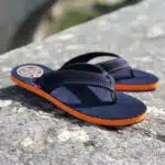 une paire de tongs bleu marine avec semelle orange et courroie bleue posée sur un muret