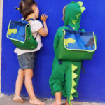 Dos enfants avec cartable (dinosaure) sur le dos
