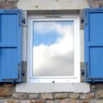 Volets battants bleu clair avec reflet du ciel dans la fenêtre
