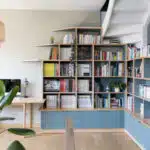 Etagère en bois clair-et peinture bleue dans salon avec lustre et plante verte.