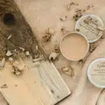 2 pots de cosmétique ronds posés sur du sable à côté d'une planche en bois
