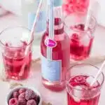 bouteille de limonade framboise avec 3 verres avec des pailles et des framboises